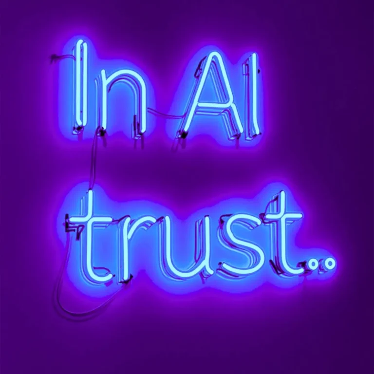 La imagen muestra un letrero de neón con luces azules brillantes y un resplandor púrpura alrededor de las letras. El texto iluminado dice: “In AI trust..”. Los tubos de neón están conectados por cables visibles que refuerzan el aspecto industrial y moderno. El conjunto transmite un mensaje futurista y tecnológico, con un aire de confianza en la inteligencia artificial. El contraste entre el fondo oscuro púrpura y la luz azul intensa hace que las palabras resalten con mucha fuerza visual.